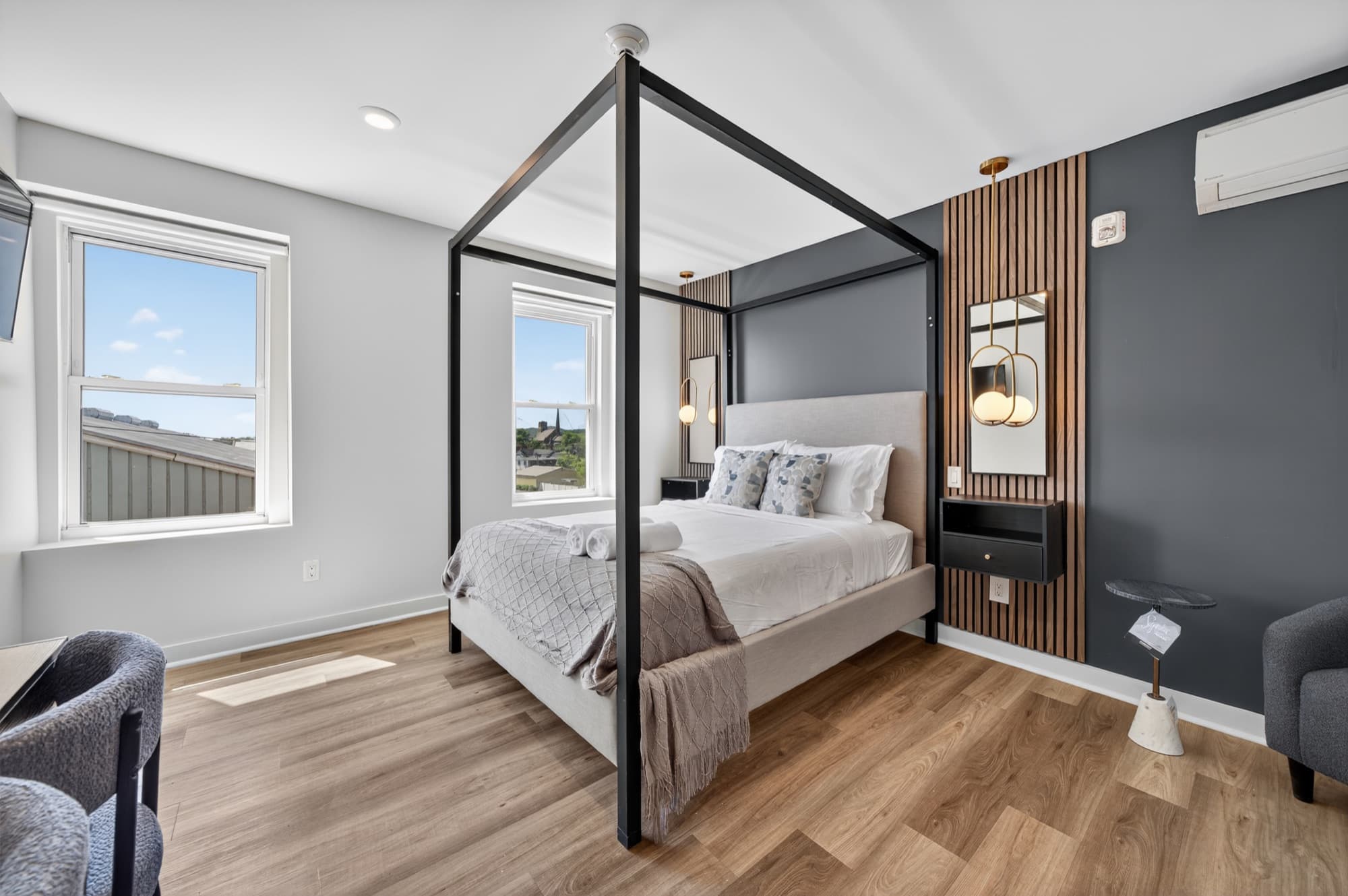 A suite at The Columbus Hotel, a black four-poster bed against a dark wall with a wood-slat panel, a window on the left