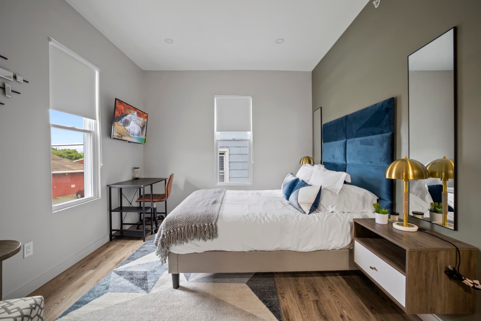A standard suite: a queen bed with a blue headboard between two windows