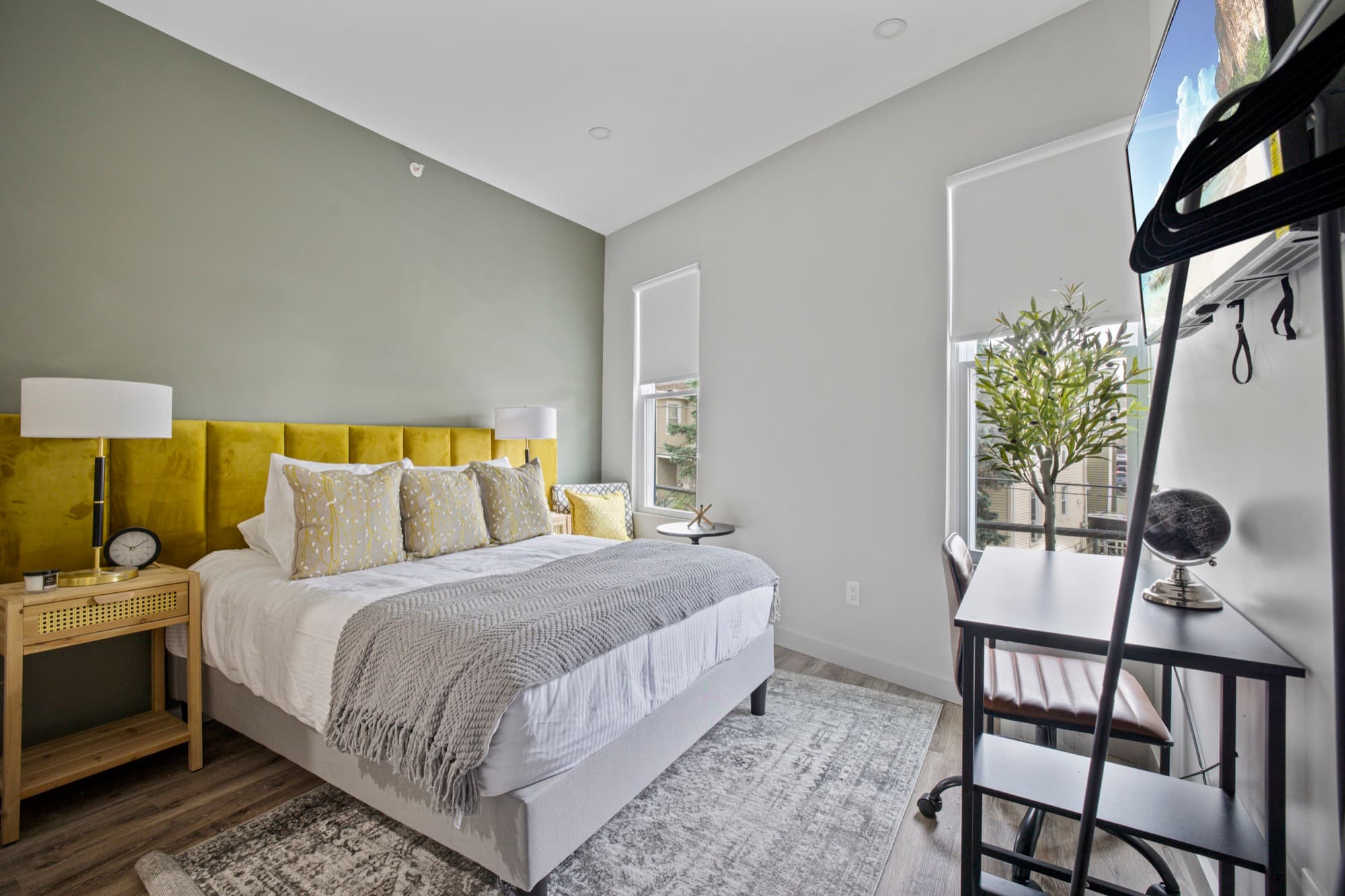 Sun-drenched bedroom with an olive headboard and two large windows