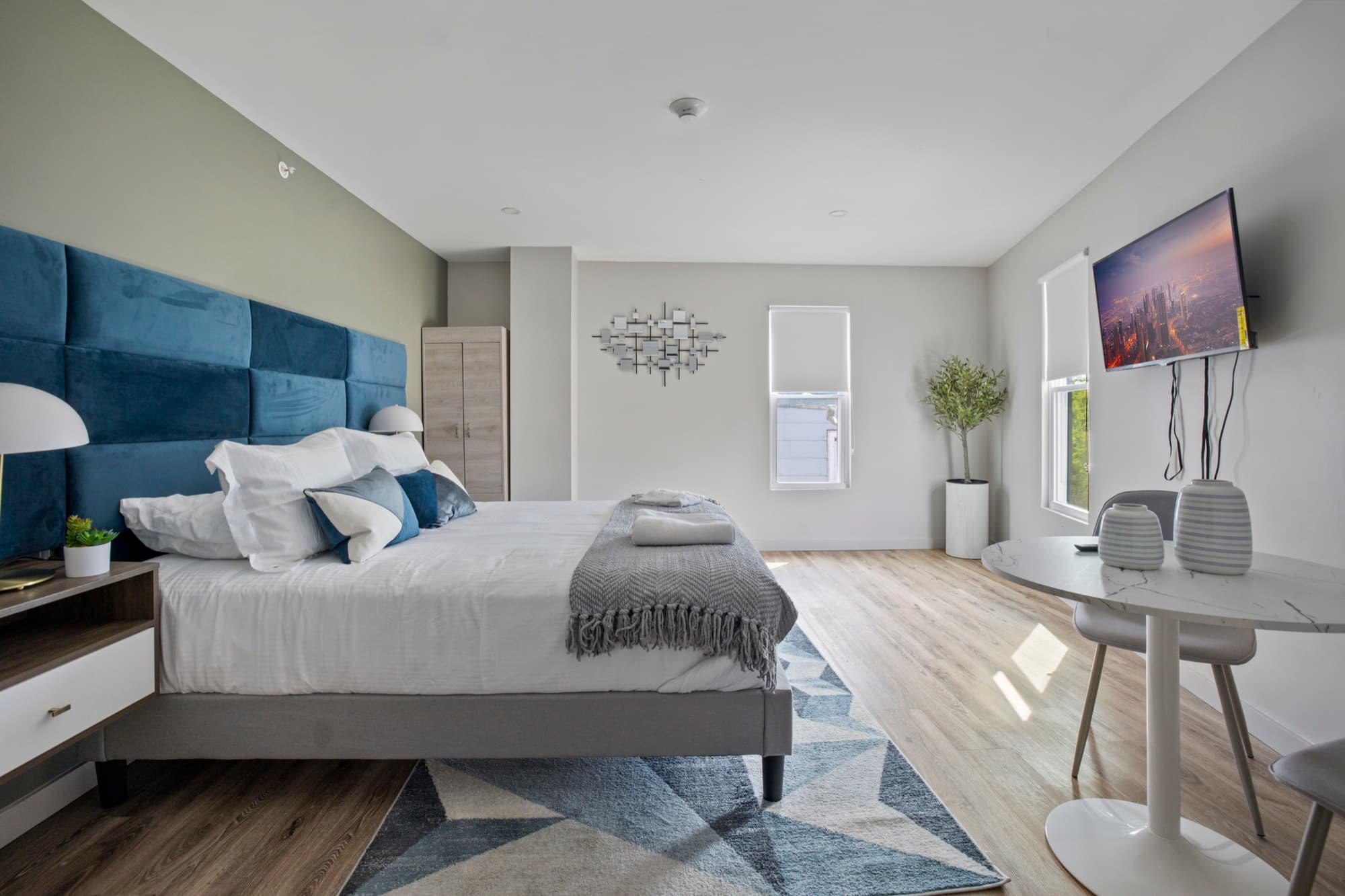 Bright, spacious bedroom with a blue velvet headboard and dining table